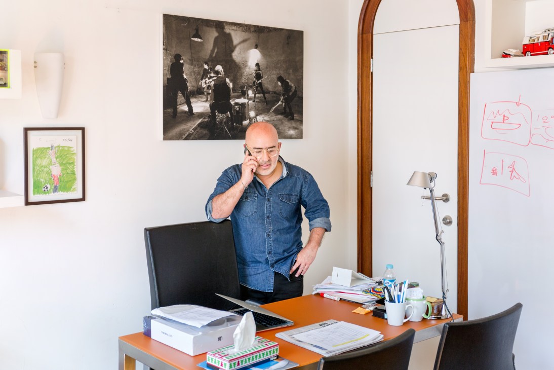 Raúl Cardós stands in his office, talking on the phone while working at an orange desk.