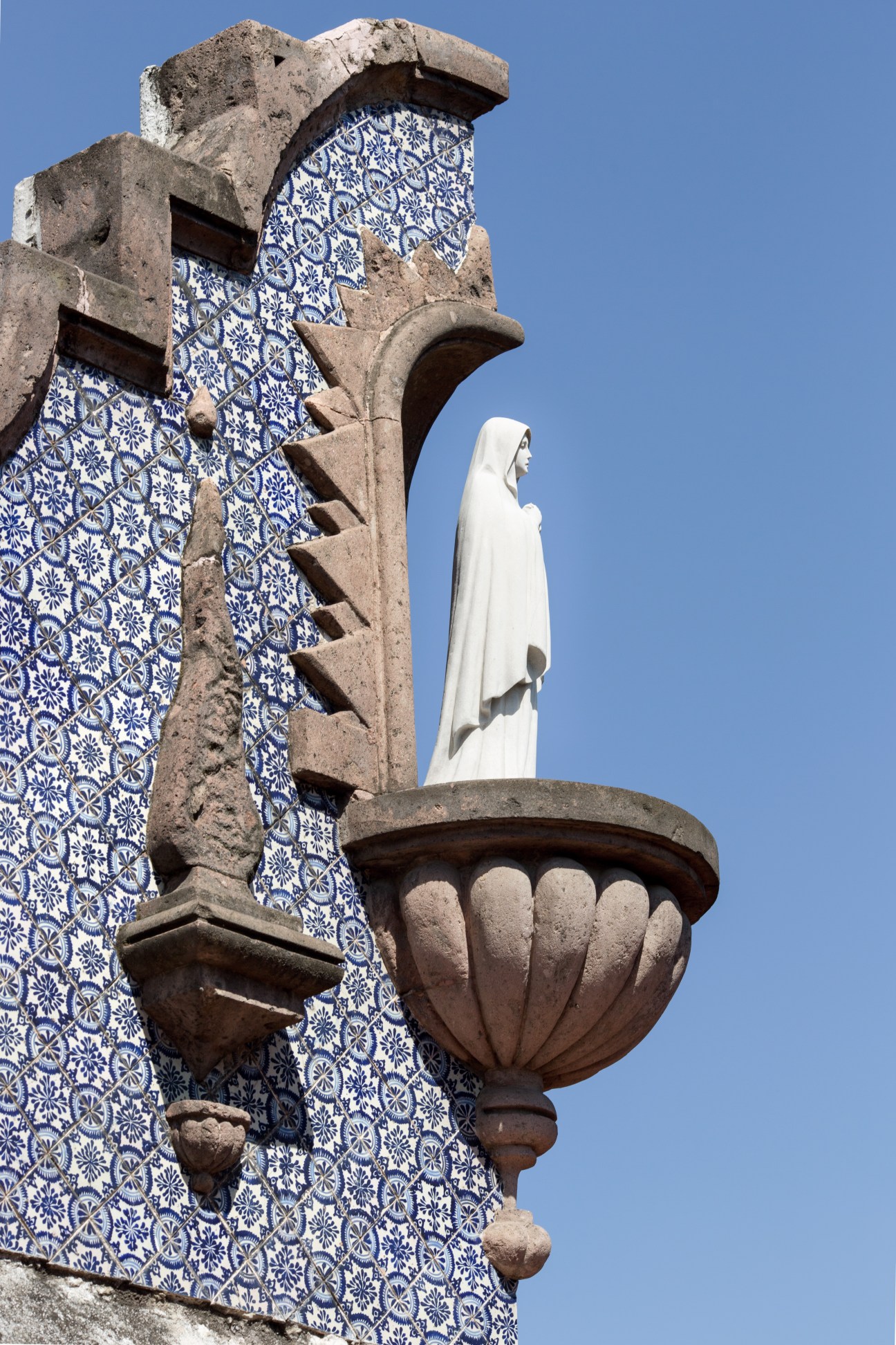 White marble religious statue beside ornate stone architecture with blue and white patterned tilework.