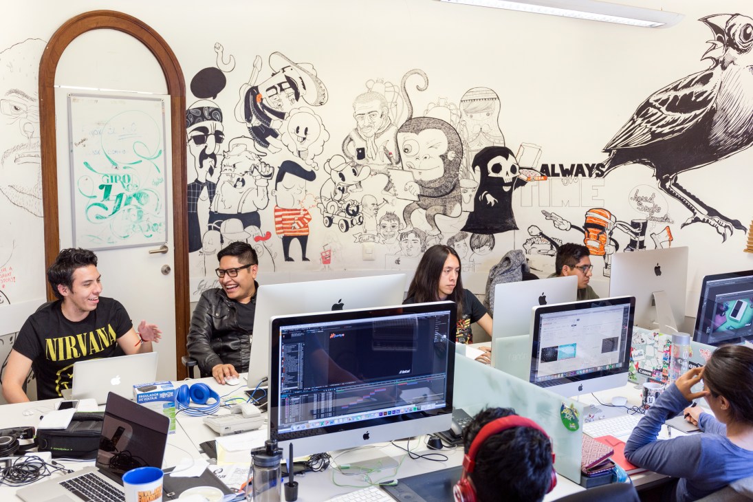 Motion graphic designers work at computers in a creative office space with illustrated wall art.