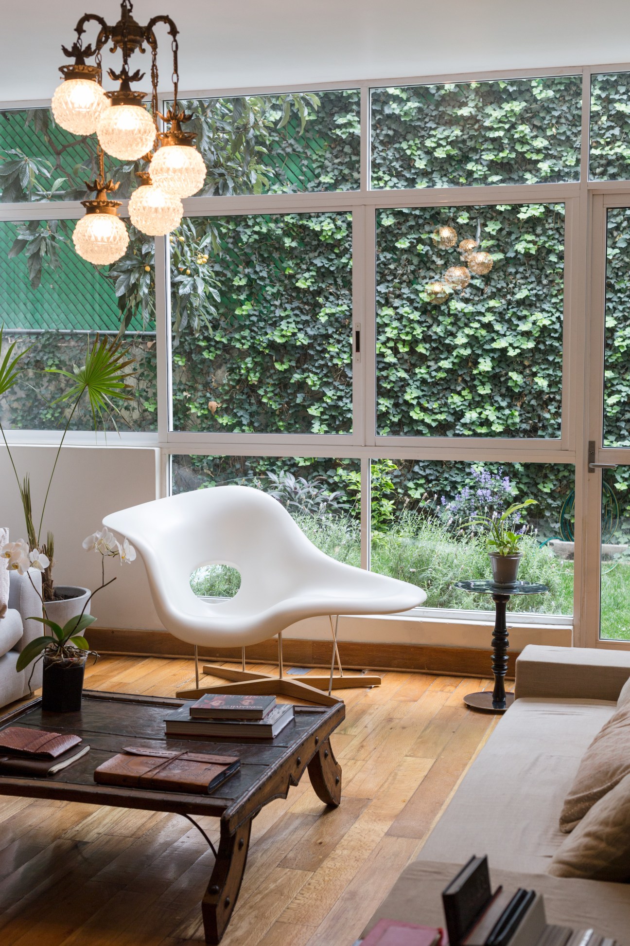 Modern living room with white sculptural chair, wooden table, and large windows overlooking a garden.