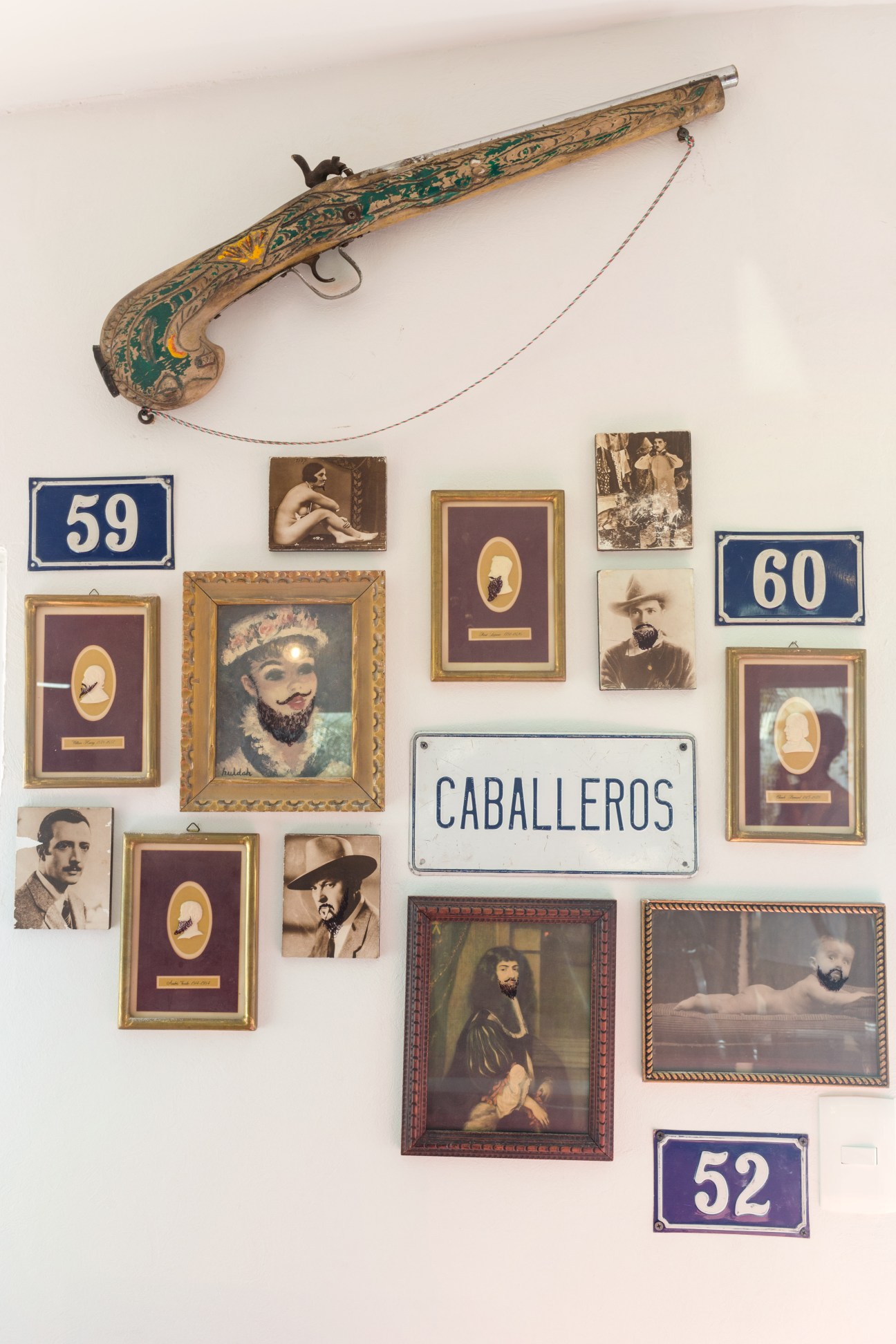 Ornate antique pistol and framed portraits displayed on a white wall in a barbershop.