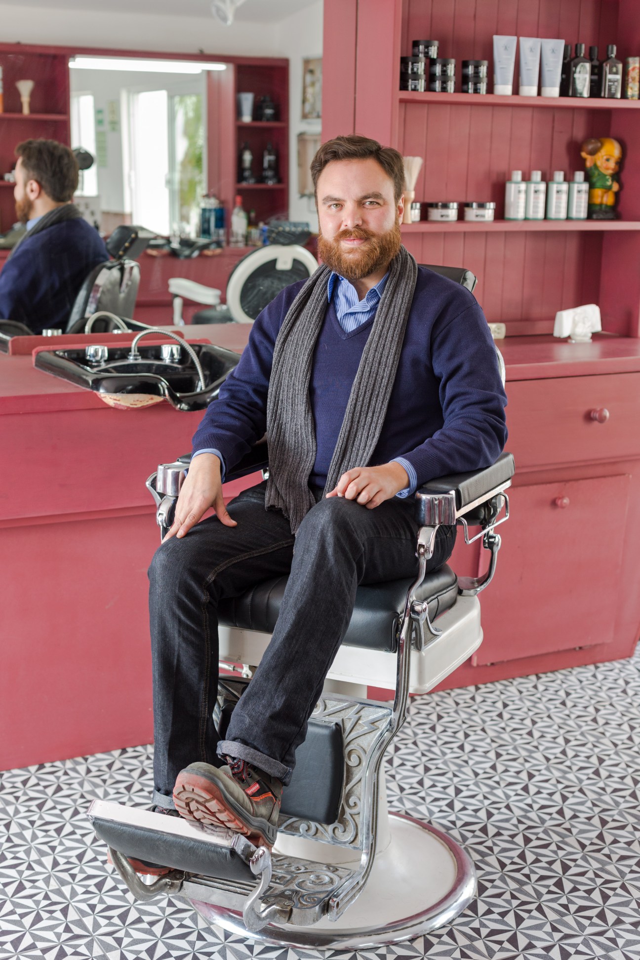 Dan Lastre, manager of the barber shop in Common People, sits in a vintage barber chair in the red-walled shop.