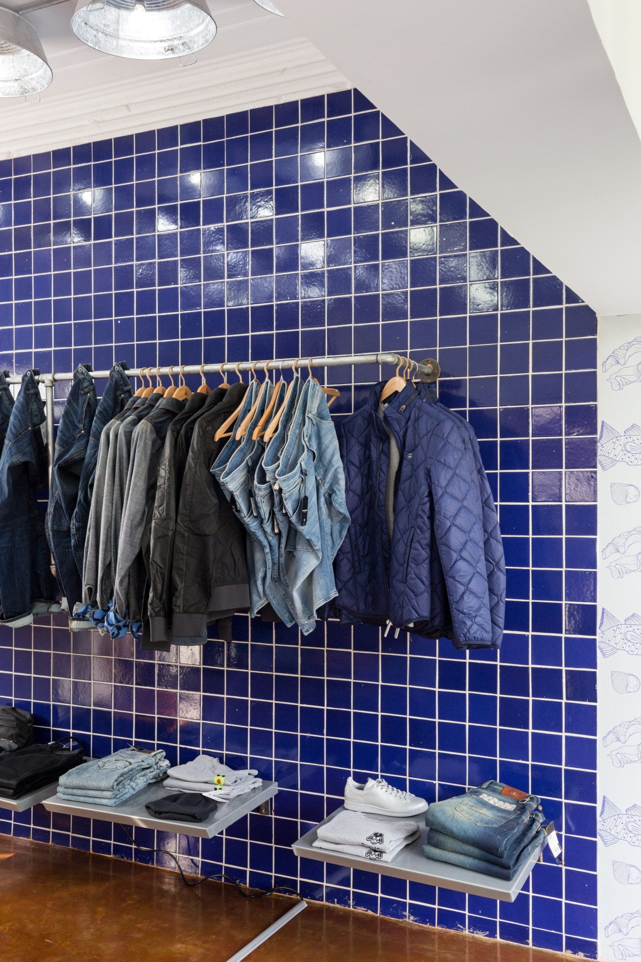 Common People clothing store display with blue tiled wall, wooden clothing racks, and folded items on shelves.