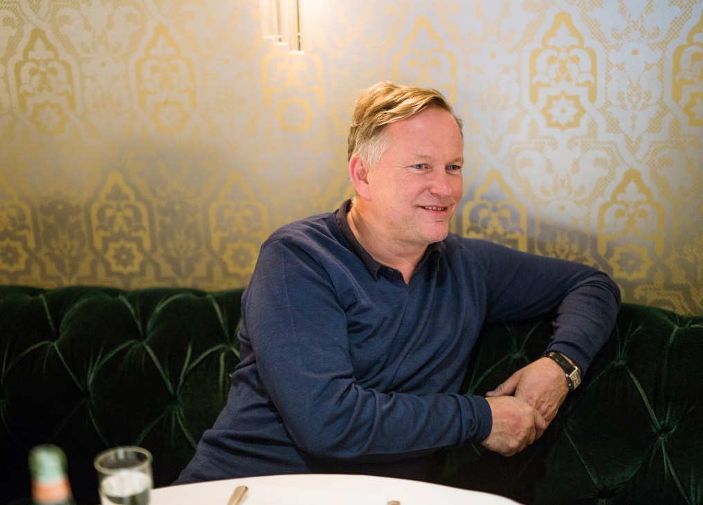 Nick Jones seated at a green velvet banquette at Cecconi's restaurant, smiling while seated at his favorite table.