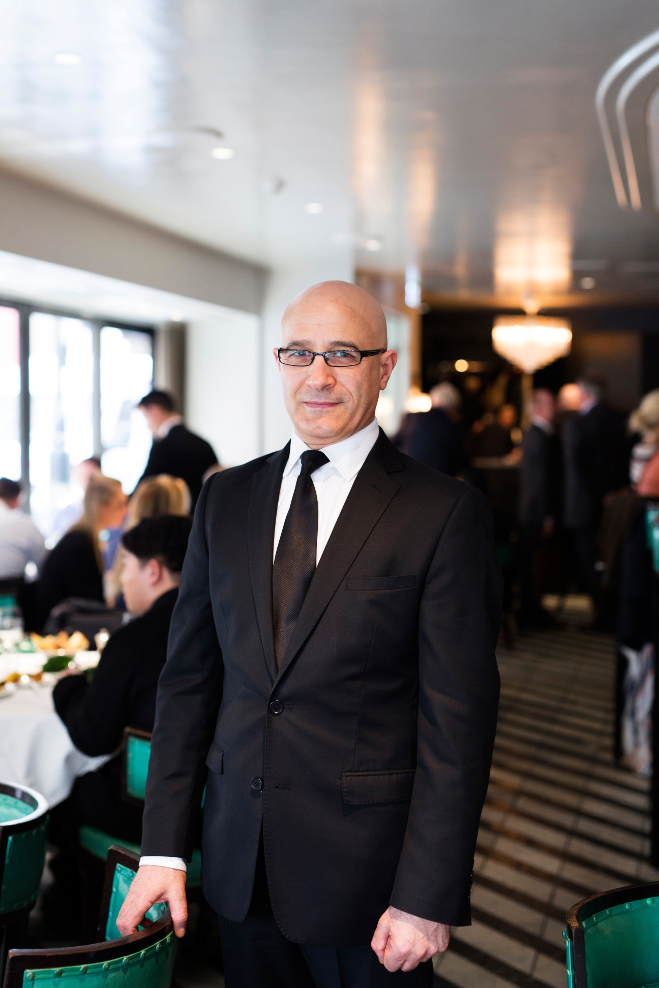 Giacomo Maccioni standing in Cecconi's restaurant wearing a dark suit and glasses.