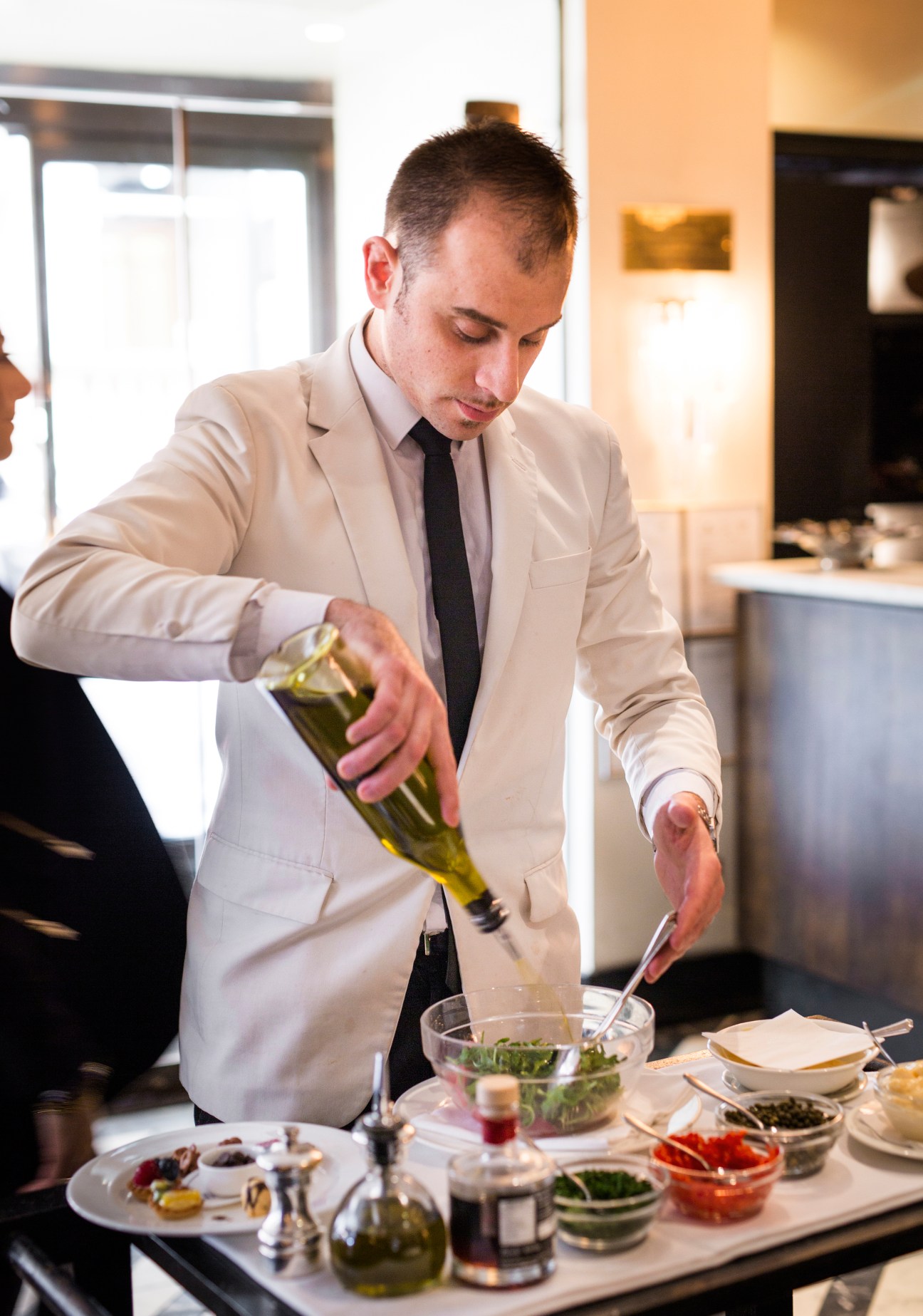 Waiter in cream blazer drizzling olive oil over salad at Cecconi's restaurant.