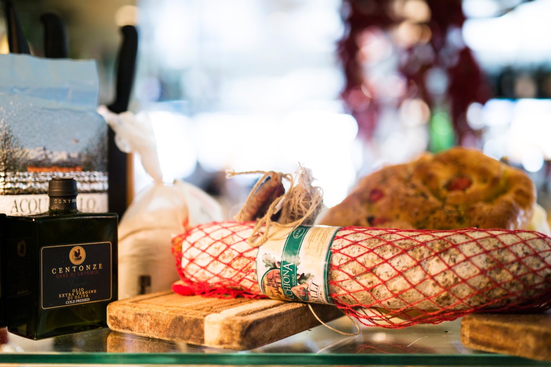Cured salami in red mesh netting next to a bottle of Centonze extra virgin olive oil on a wooden board at Cecconi's restaurant.