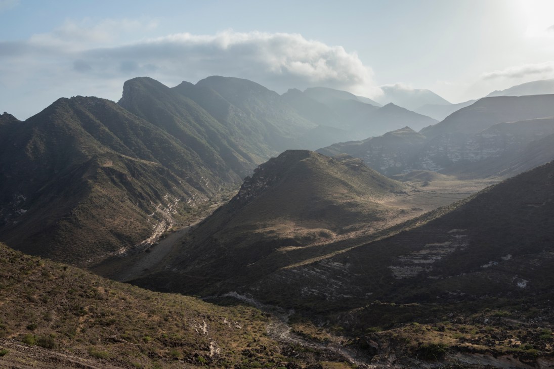 The Dhofar Mountains in Oman with layered peaks, a river valley, and lush green vegetation during monsoon season.
