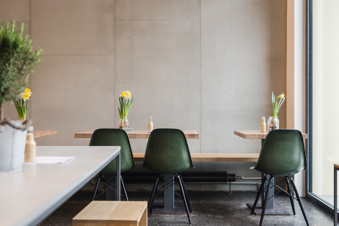 Minimalist restaurant interior with green chairs at wooden counter and yellow daffodils in glass vases.