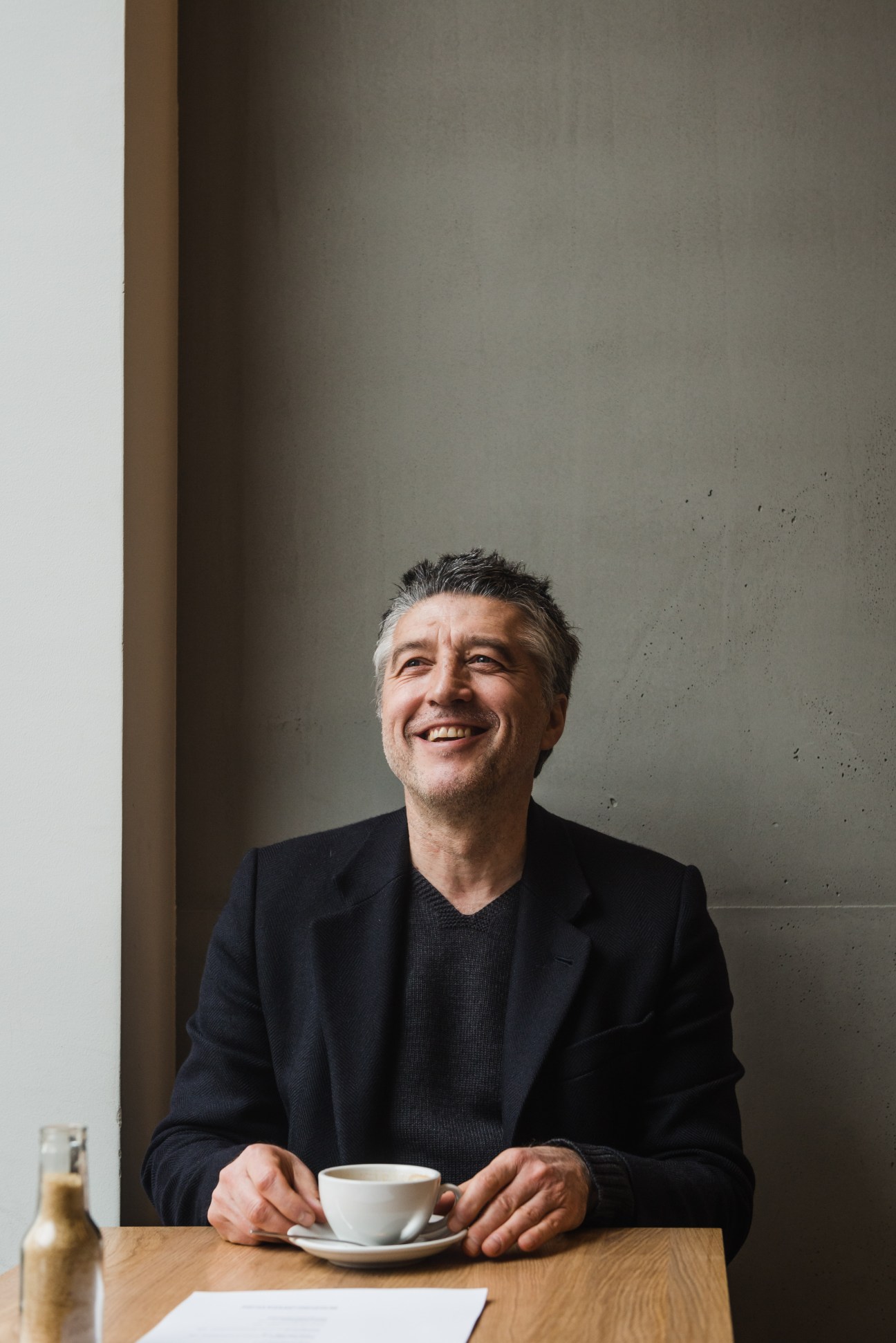 Andreas Murkudis sits at a table with a white cup of coffee, smiling at Oliv Eat restaurant.