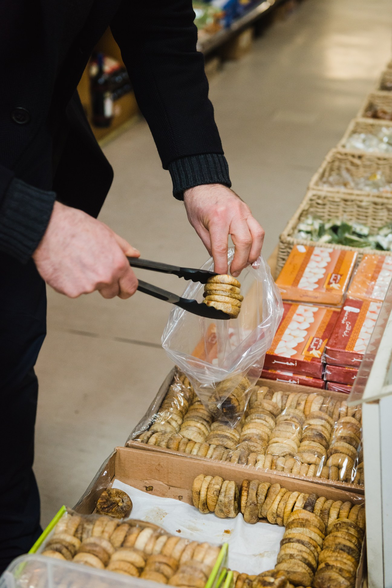 Hand using tongs to pick up pastries from a display box at Harb Lebanese shop in Berlin.
