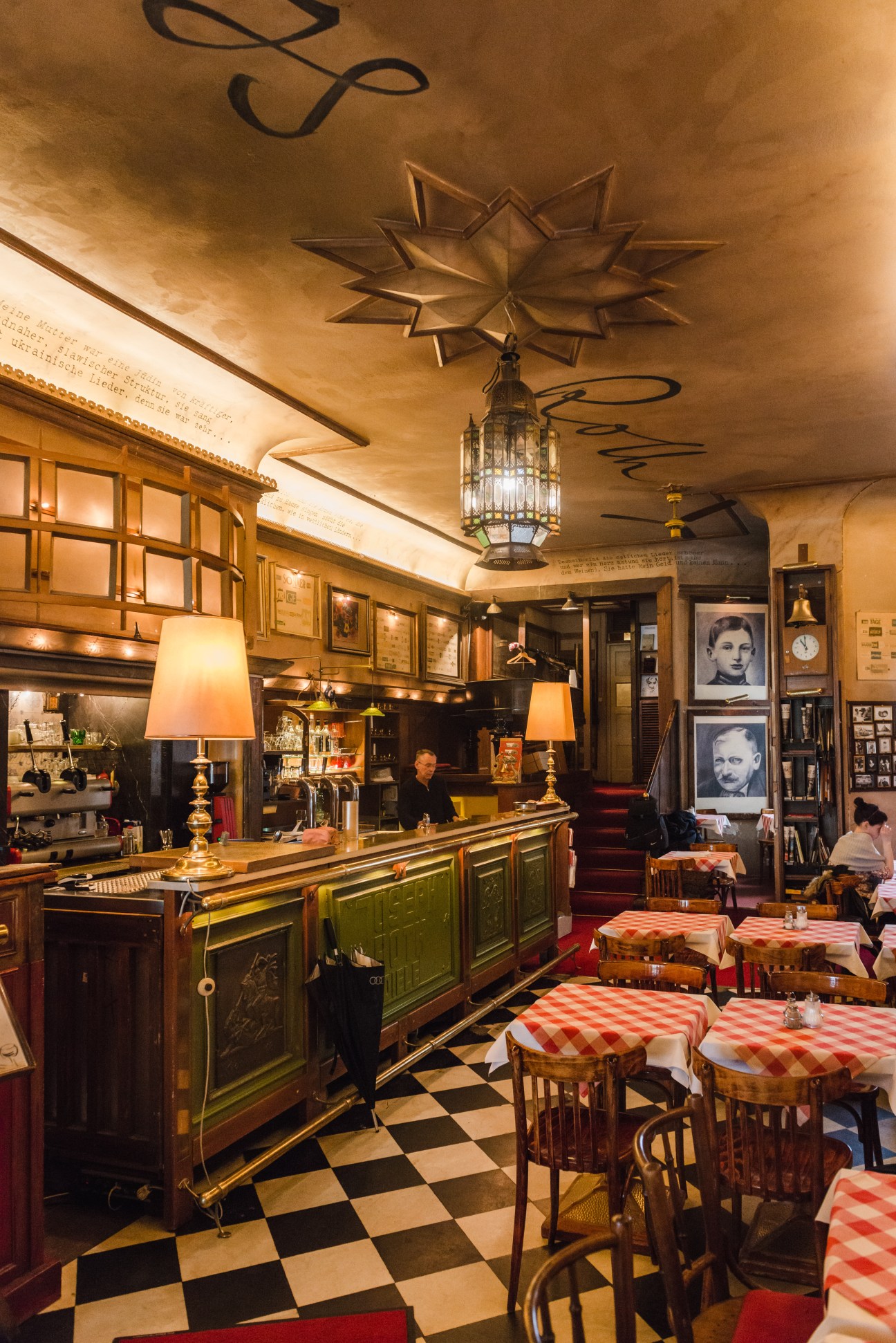 Interior of Joseph Roth Diele restaurant with warm wood paneling, brass fixtures, checkered tablecloths and pendant lighting.
