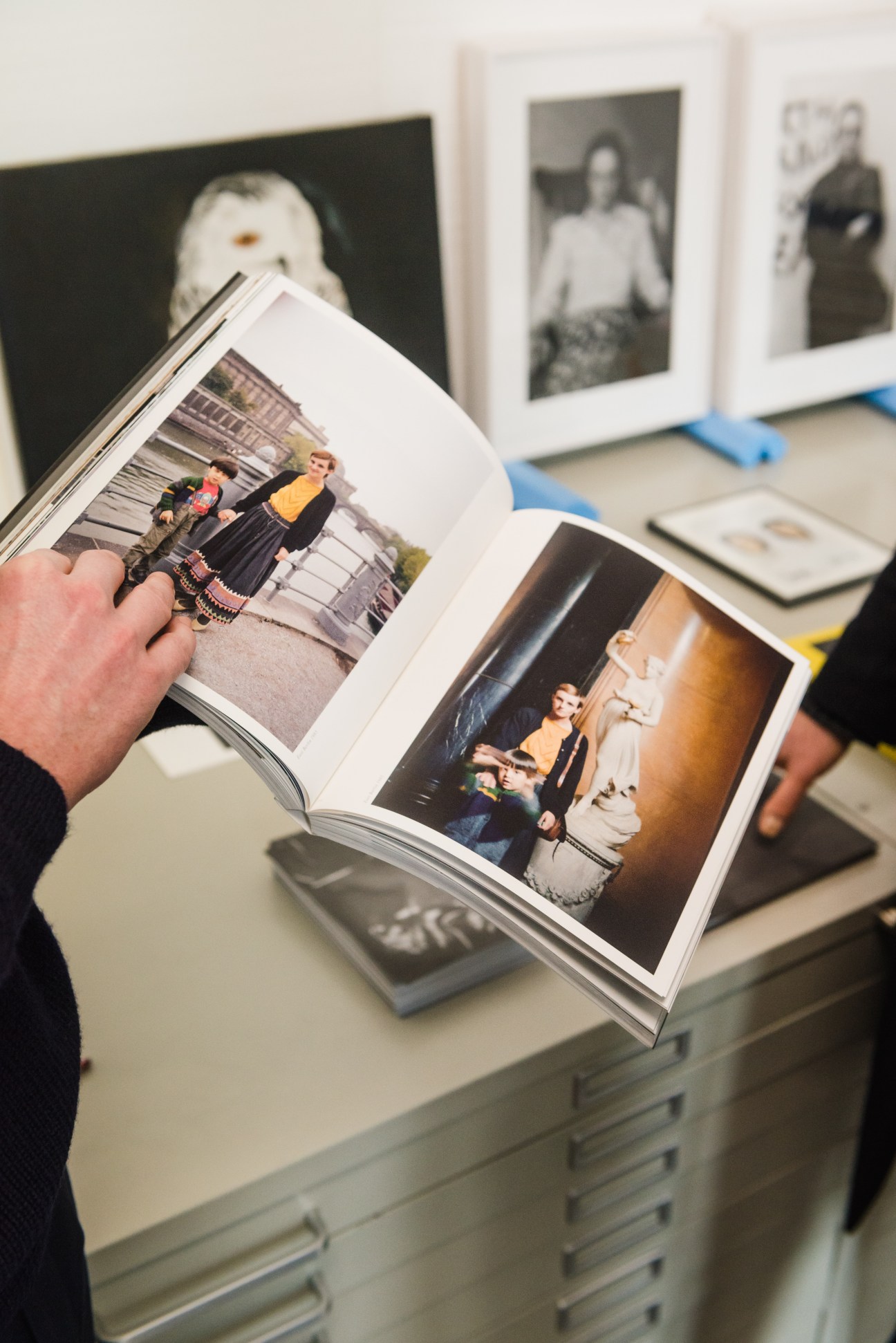 Hand holding open a photography book displaying images of people in an interior space at Thomas Fischer gallery.