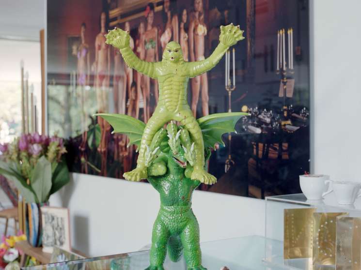 A vintage green plastic creature toy with raised arms displayed on a glass table among eclectic home decor.