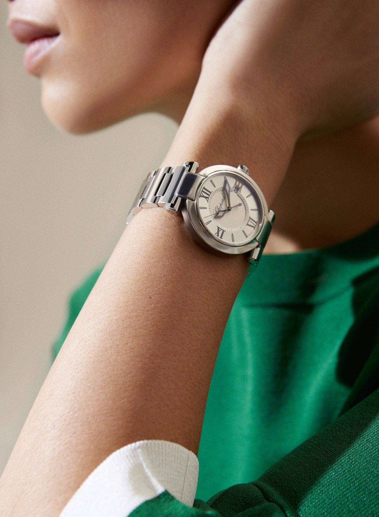 Silver stainless steel watch with Roman numerals worn on a wrist against a green sleeve.