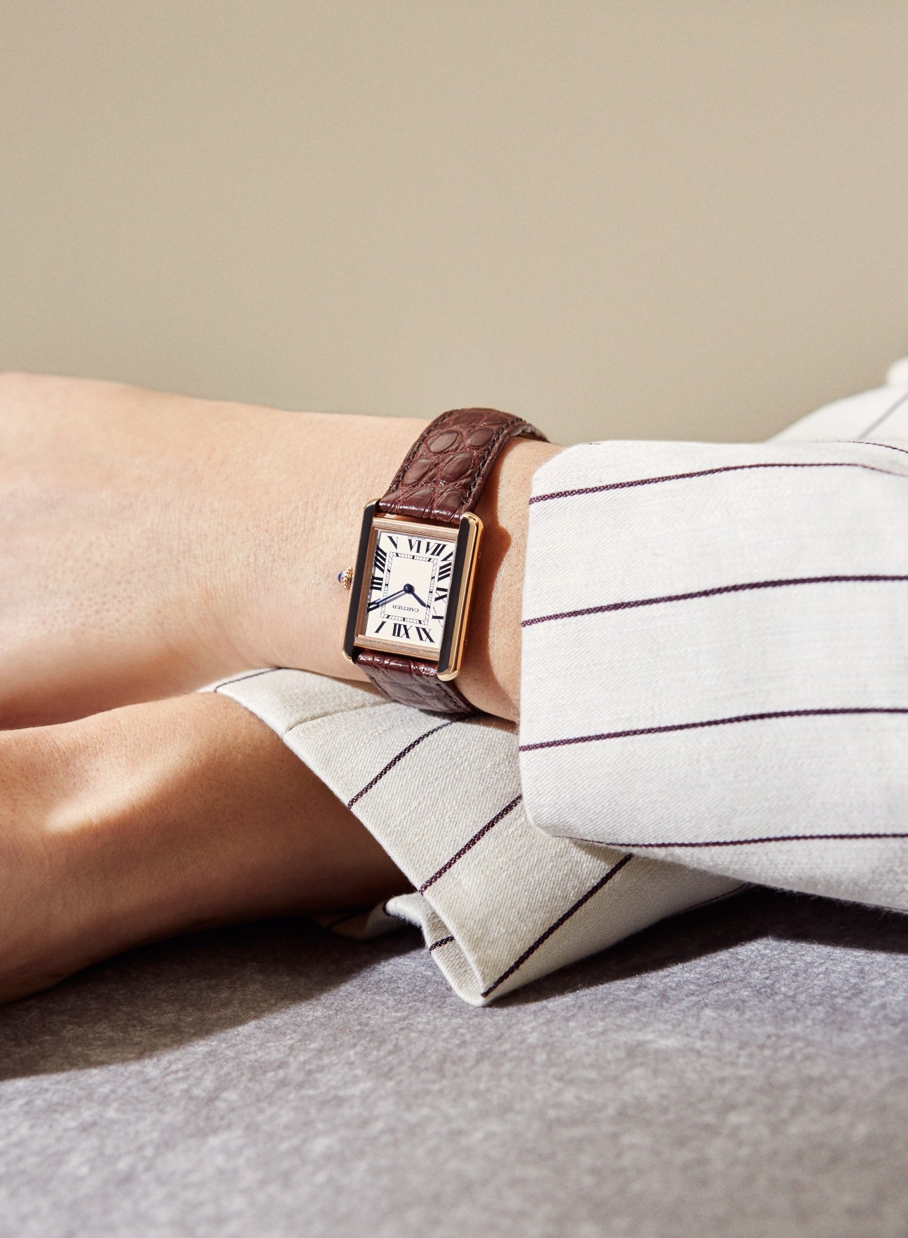 Tank Solo in pink gold by Cartier watch worn on wrist with brown leather strap and white striped shirt.
