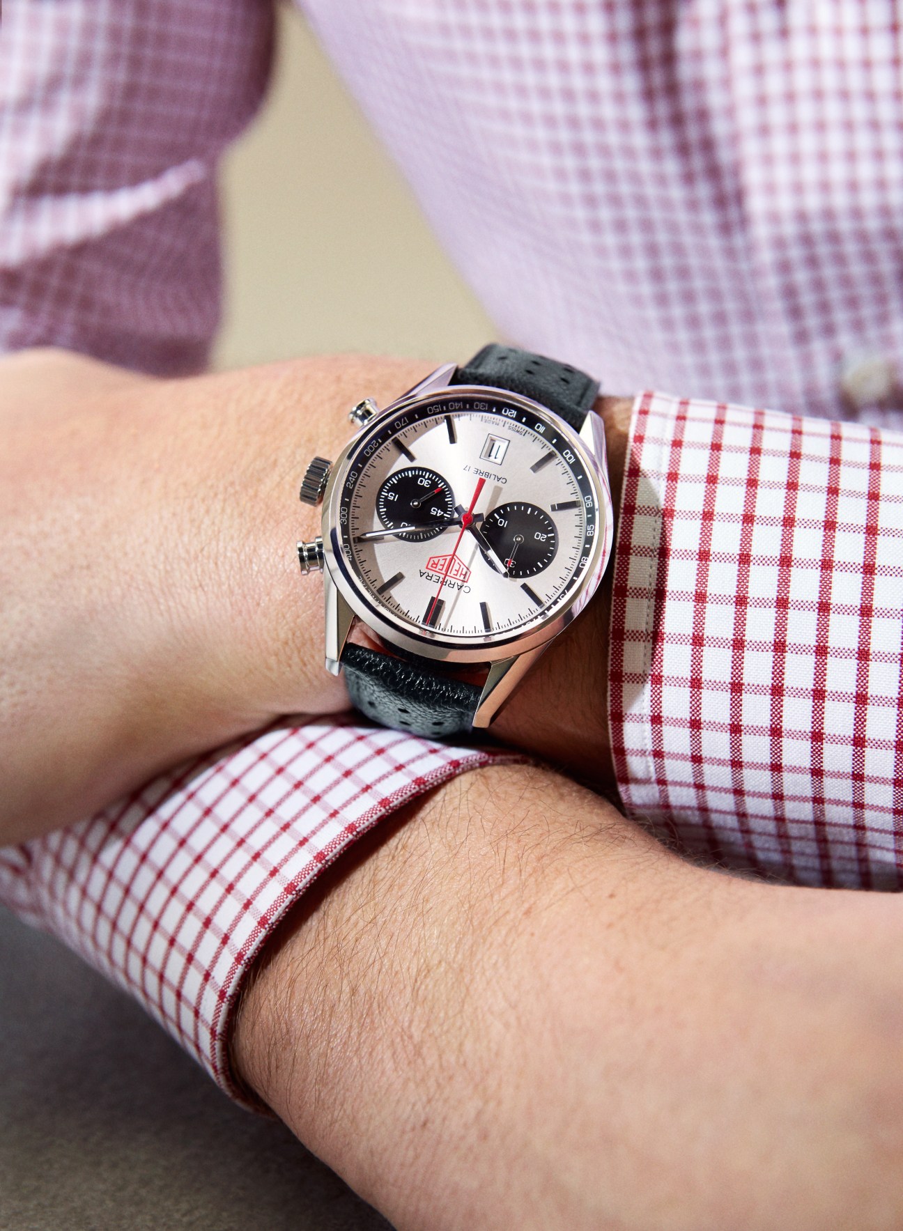 Tag Heuer Carrera panda chronograph watch with white dial and black subdials worn on wrist with red and white checkered shirt cuff.