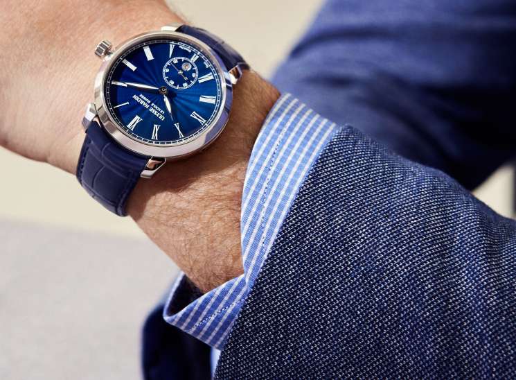 Classico manufacture grand feu watch by Ulysse Nardin with blue dial and leather strap worn on wrist with blue striped shirt cuff.