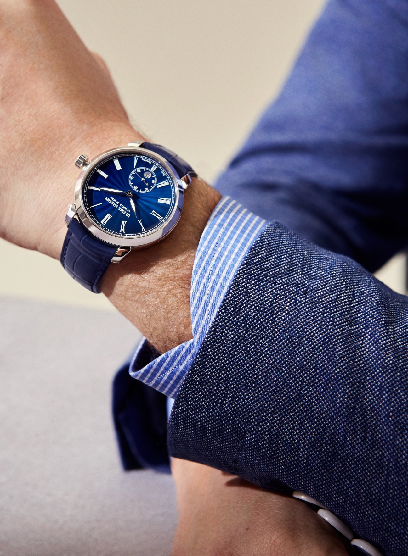 Classico manufacture grand feu watch by Ulysse Nardin with blue dial and leather strap worn on wrist with blue striped shirt cuff.