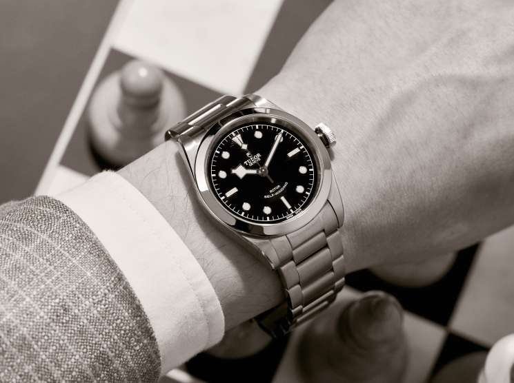 Heritage Black Bay 41 by Tudor watch with black dial on wrist wearing white cuff and gray jacket.