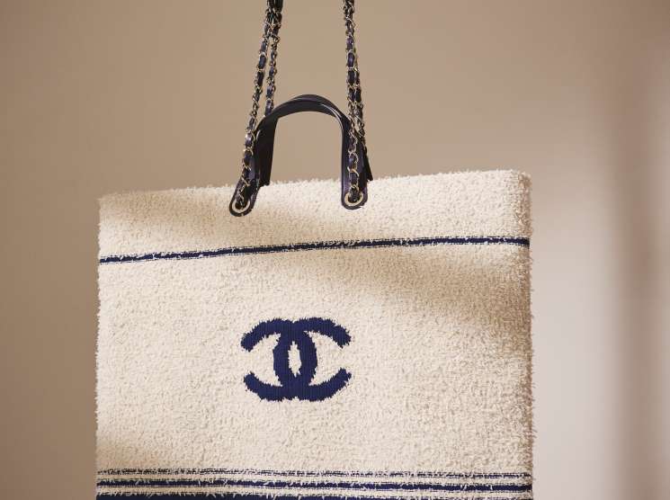 Chanel tote bag in cream and navy textured fabric with interlocking CC logo held by a model's hand.