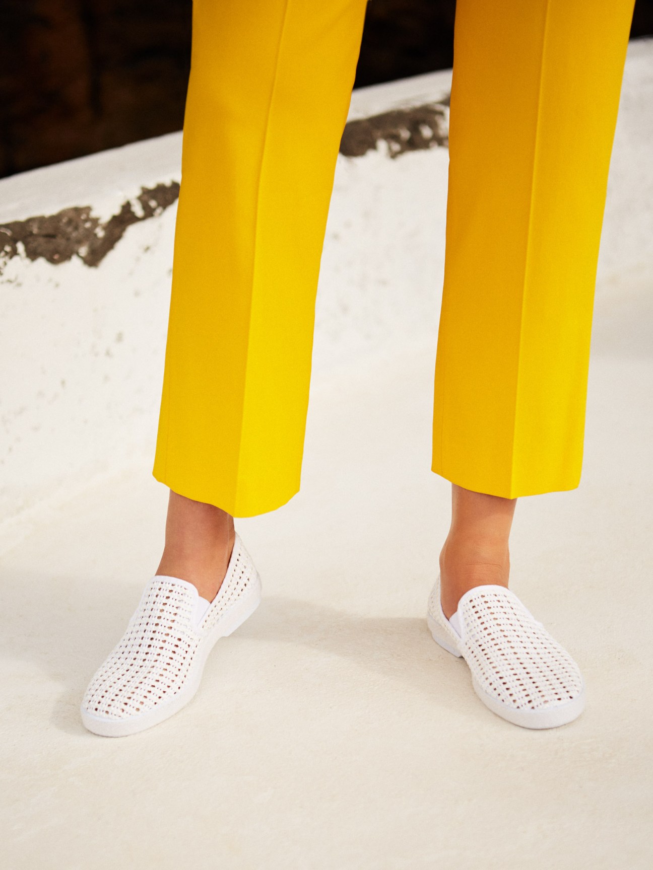 Person wearing bright yellow cropped trousers by Maison Rabih Kayrouz and white perforated slip-on sneakers by Rivieras.