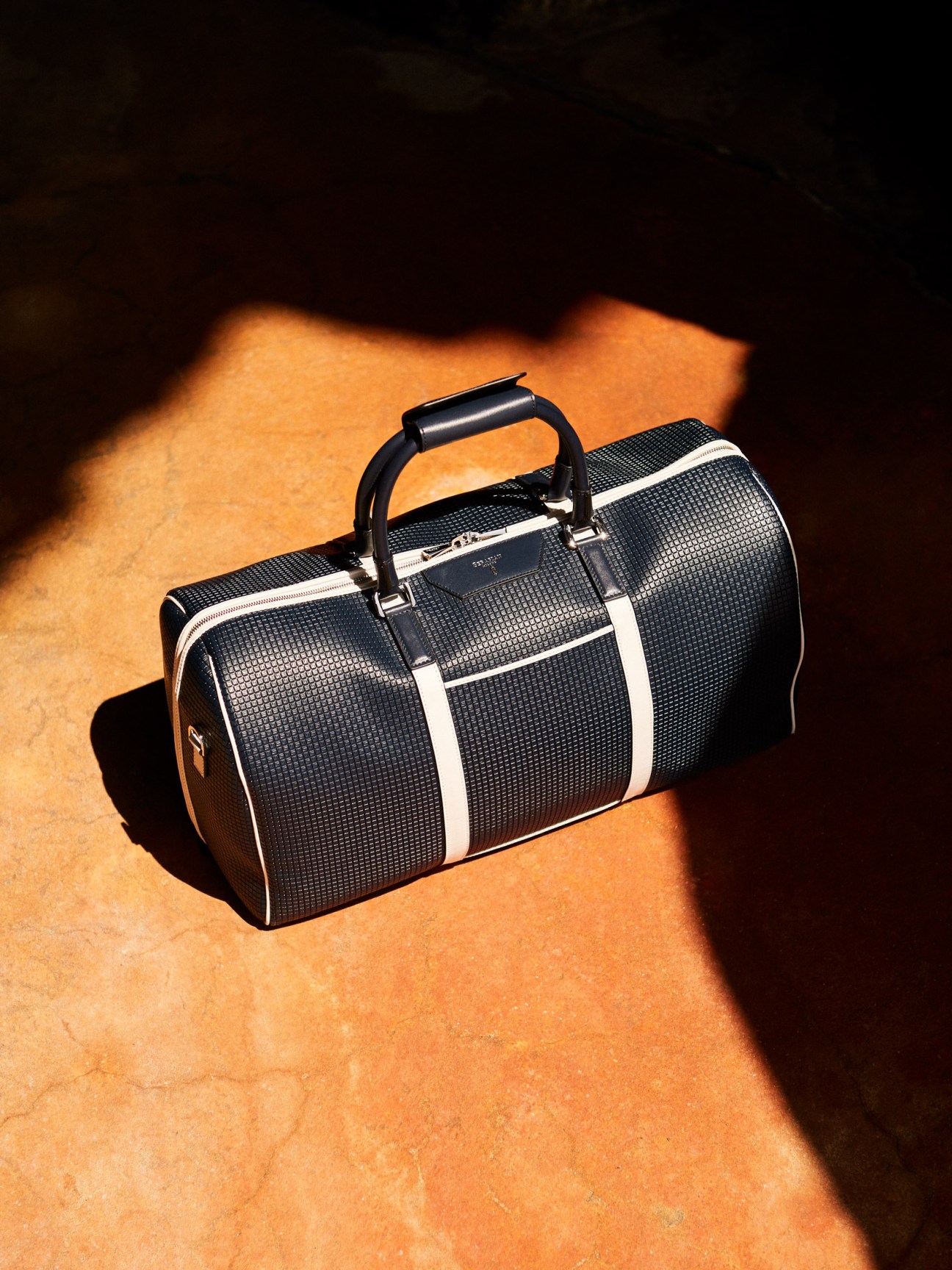 Black textured Serapian travel bag with white stripes and black handles on terracotta ground.