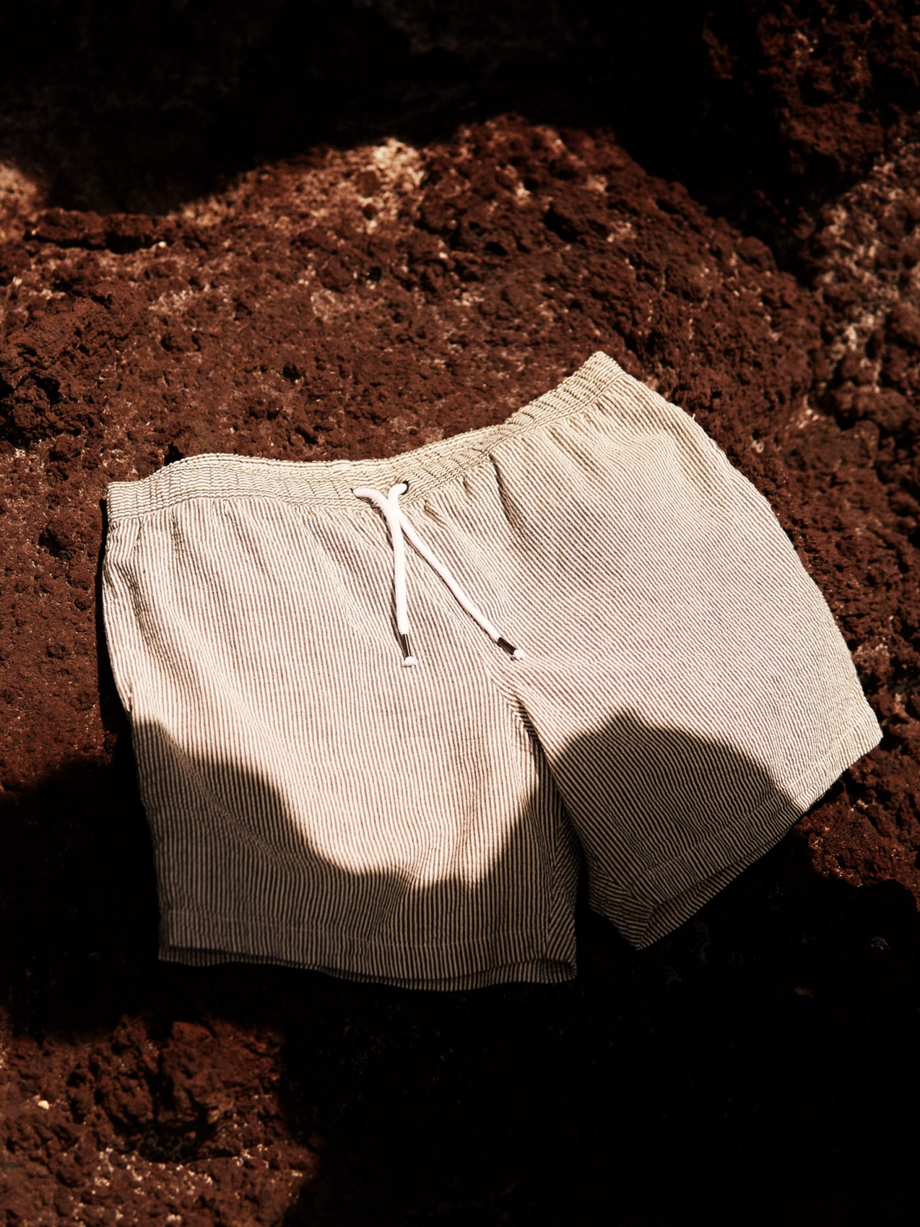 Cream ribbed swim shorts by Aspesi laid on brown earth.