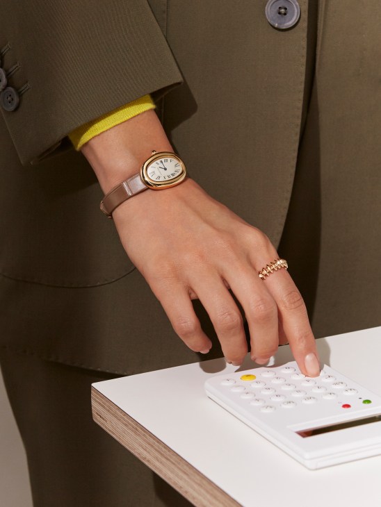 Hand wearing a Cartier Baignoire 1920 watch and ring, resting on a calendar, styled with a Pal Zileri suit.