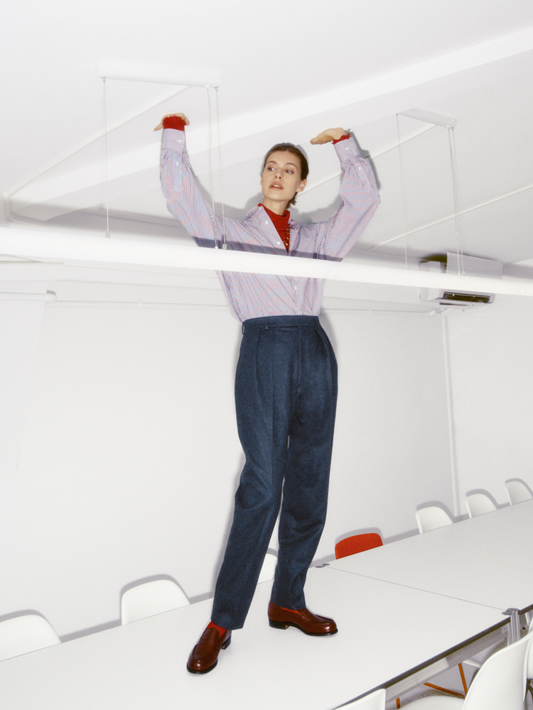 Person in striped shirt, navy trousers, and red accessories poses with arms raised on white boat deck