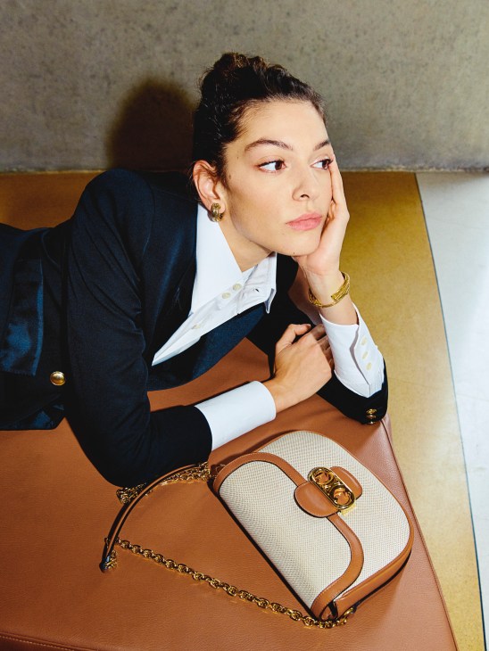 Woman in navy Saint Laurent jacket and white shirt with gold earrings and bracelet, holding a Celine bag.