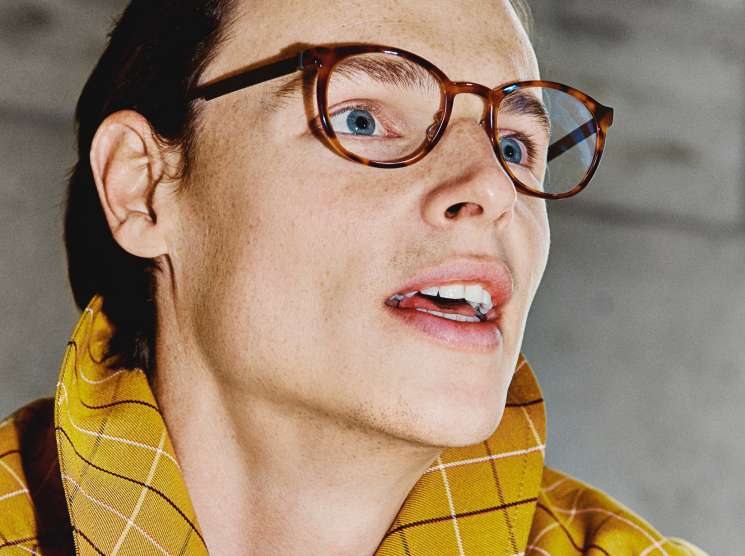 Model wearing a yellow plaid Mackintosh coat and tortoiseshell Lindberg glasses against a neutral background.