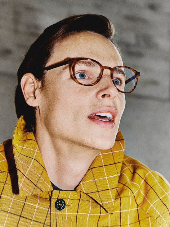 Model wearing a yellow plaid Mackintosh coat and tortoiseshell Lindberg glasses against a neutral background.