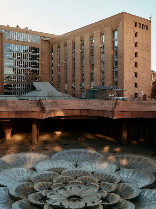 Avetik Isahakyan Central Library building with red brick facade and modern glass extension, viewed from plaza with decorative fountain.