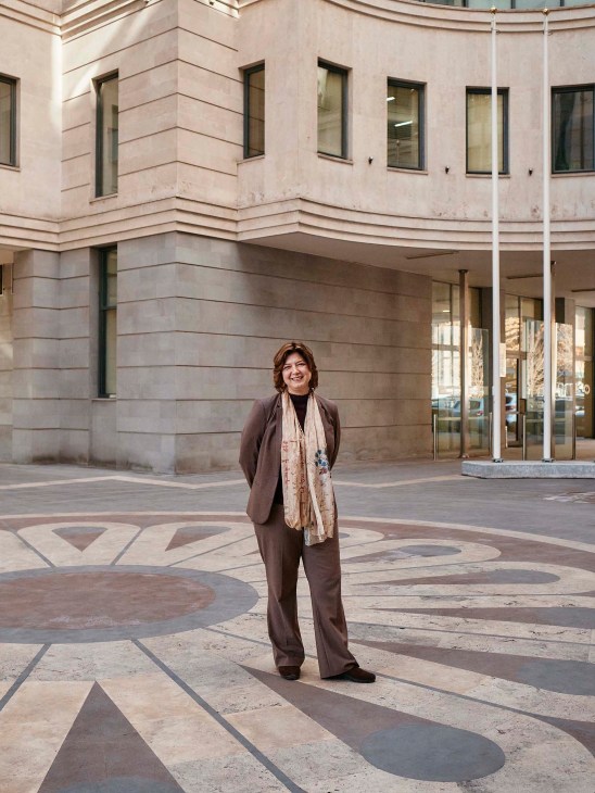 Sara Anjargolian stands in front of a modern institutional building with geometric floor patterns in Yerevan.