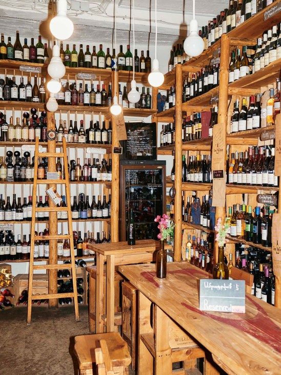 Interior of In Vino wine bar in Yerevan with wooden shelving displaying hundreds of wine bottles and pendant lights.