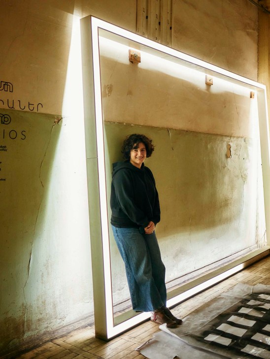 Maral Mikirditsian, head of Tumo Studios, stands in front of a large illuminated frame in an attic space.