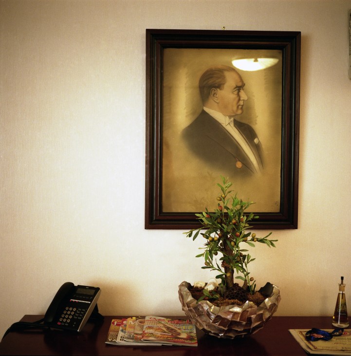 Portrait of Ataturk in ornate frame hanging above desk with phone and potted plant.