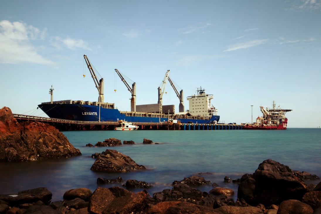 Large cargo ship named Levante docked at Dampier Port with loading cranes, surrounded by rocky coastline.
