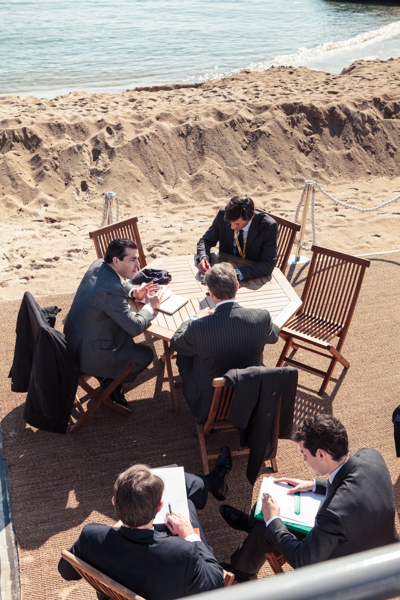 Business professionals in suits meeting on a beach near Cannes with documents and notepads.