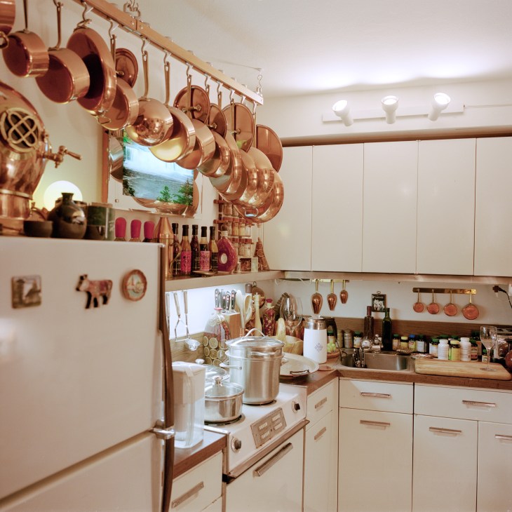 A vintage kitchen with copper pots hanging on a rod, cream-colored cabinets, and original GE-style appliances.