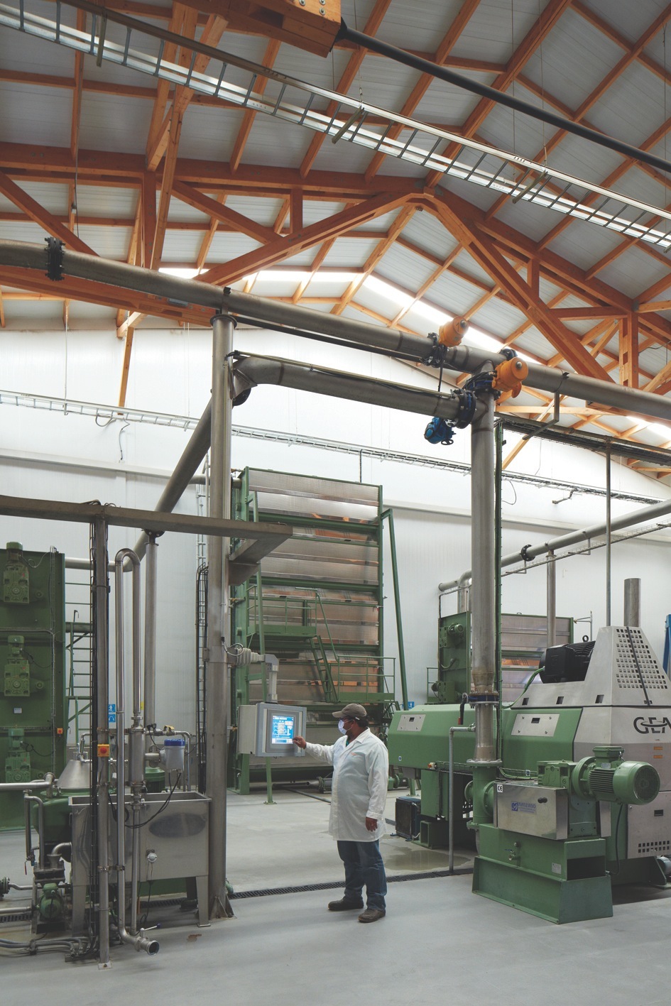 Industrial factory interior with green machinery, wooden beam ceiling structure, and worker in white coat