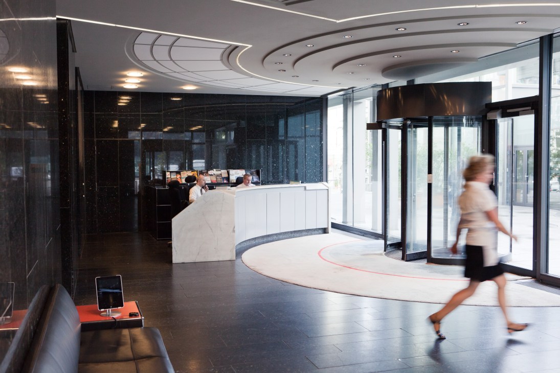 Modern reception area with curved white desk, black glass walls, and architectural ceiling with recessed lighting.