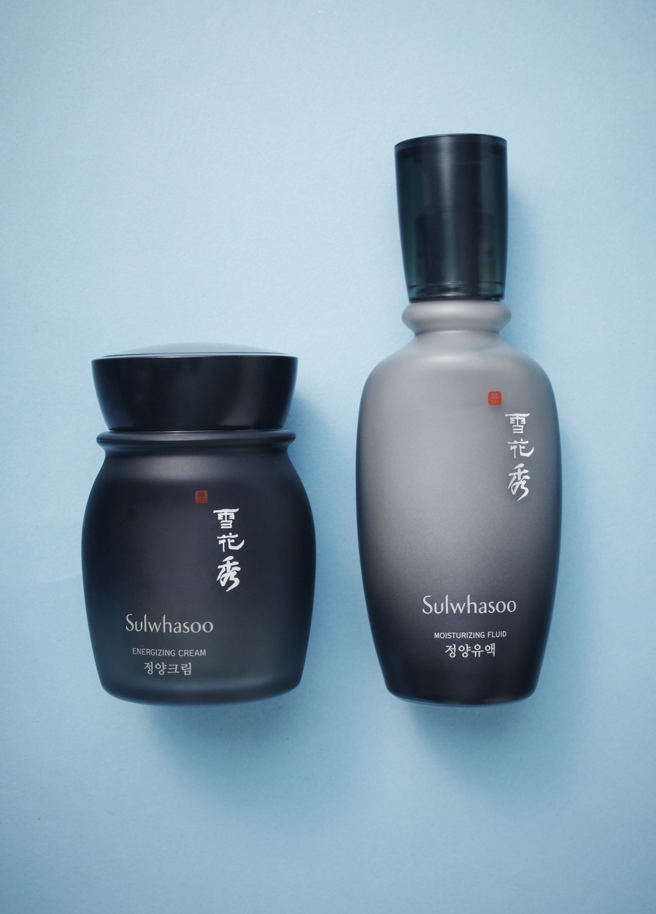 Two black Sulwhasoo skincare bottles with white text and red seals on light blue background.