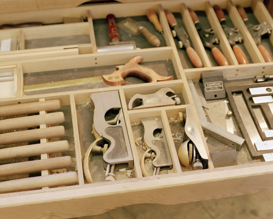 Organized wooden drawer containing various woodworking hand tools including planes, chisels, and other carpentry implements.