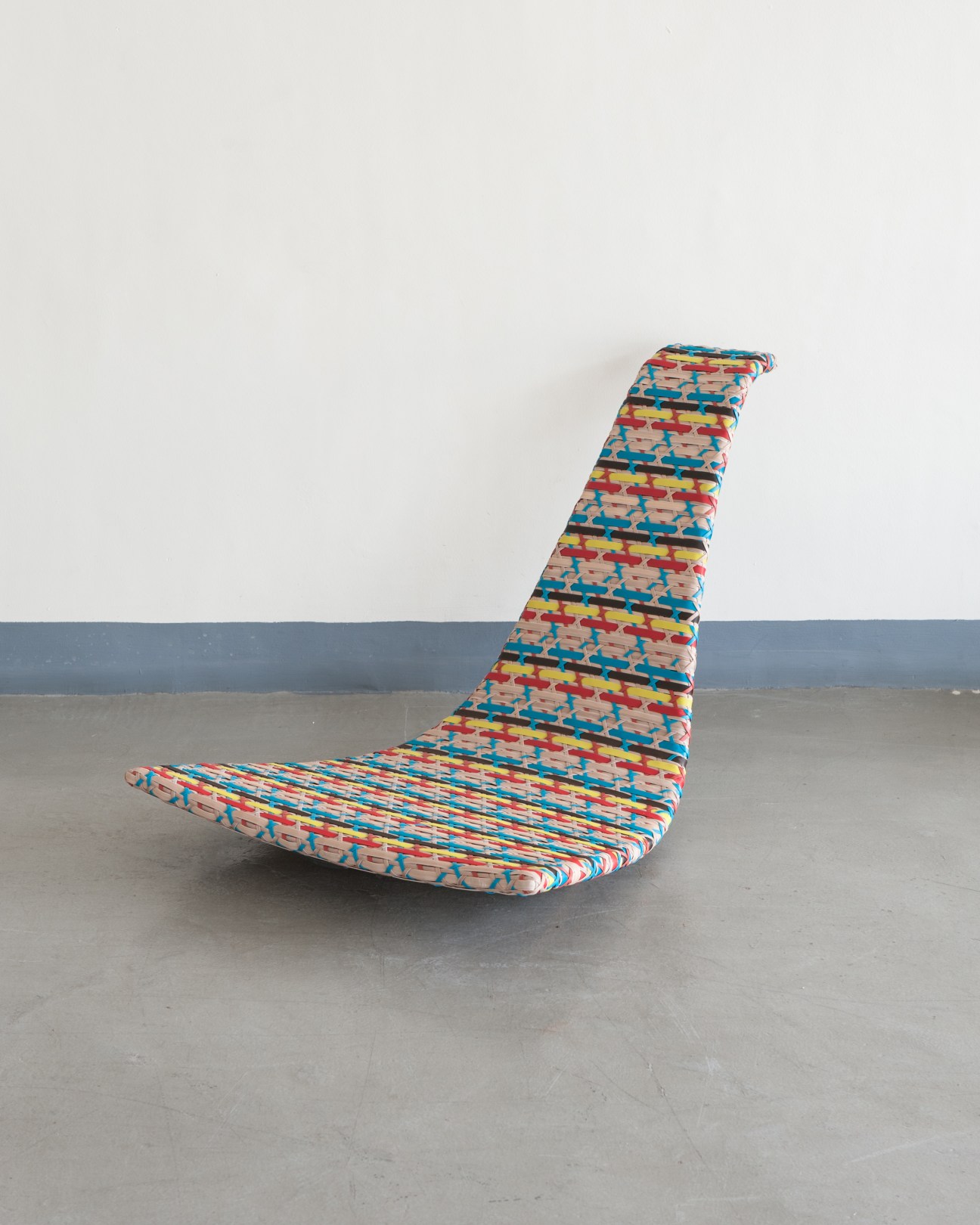 Colorful woven seat by Dedon with geometric patterns in red, blue, and yellow on concrete floor.