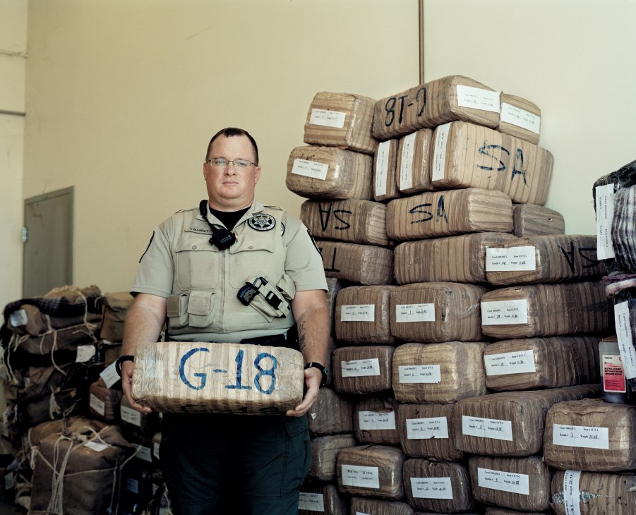 Deputy Sheriff Tim Barrett holds a package marked G-18 in front of stacked bundles of seized marijuana.