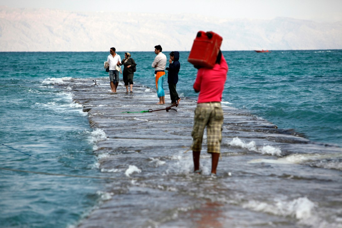 Tourists wading in Persian Gulf waters at Kish island beach with child in red shirt in foreground.