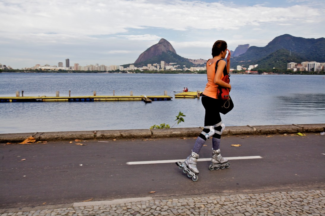 Woman rollerblading along Rio de Janeiro's lagoon track with mountains and city skyline in background.