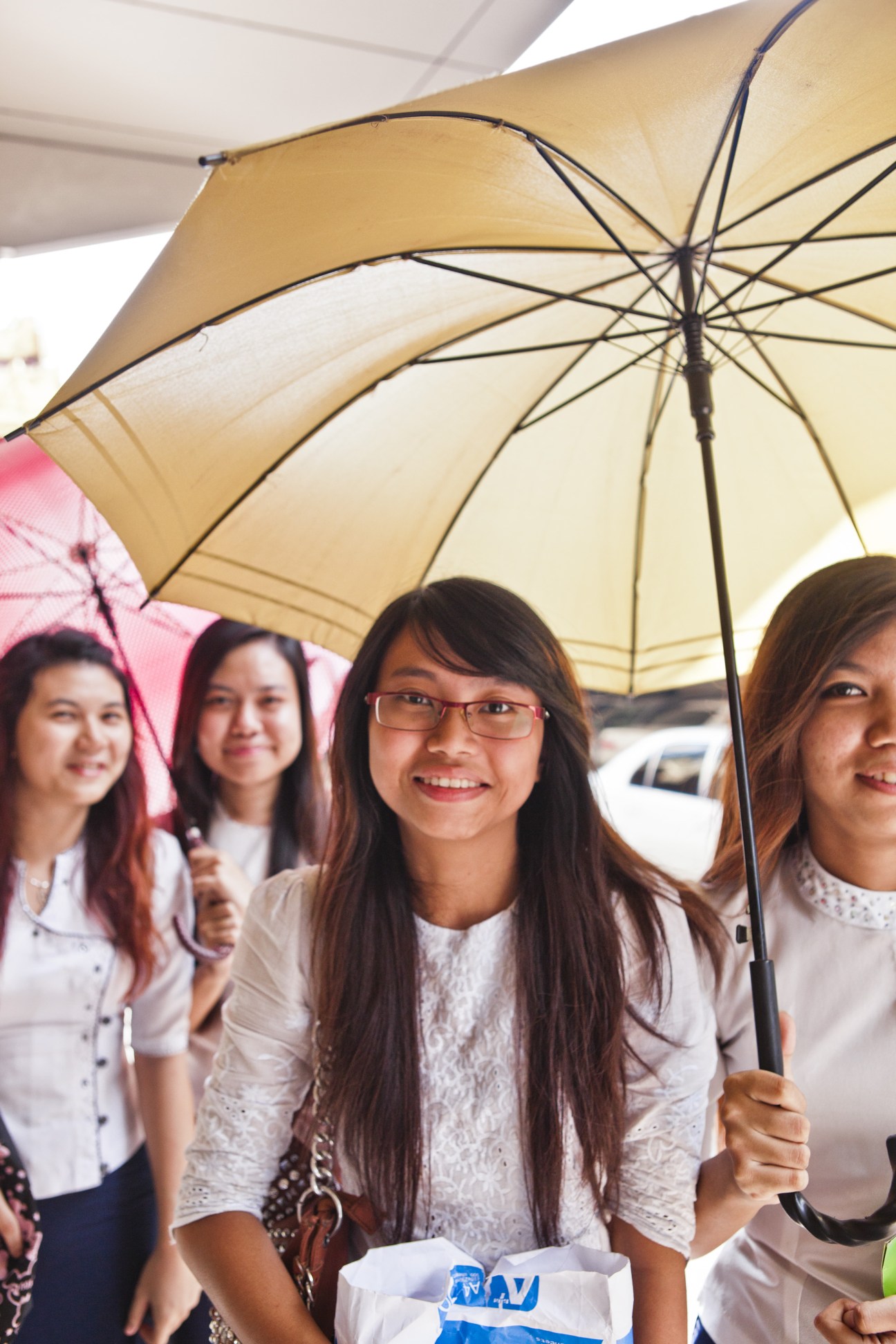 Young women in white shirts holding umbrellas during lunch break in Rangoon.